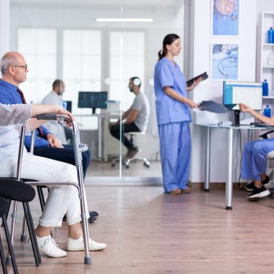 Senior woman with walking frame in hospital waiting room for rehabilitation treatment. Medical staff discussing about patient x-ray.